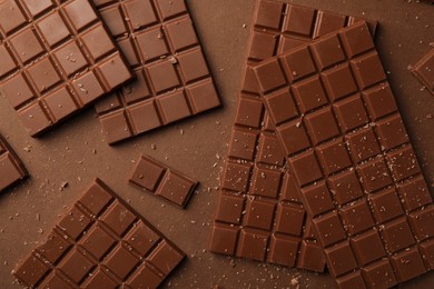 Pieces of tasty chocolate on brown background, flat lay