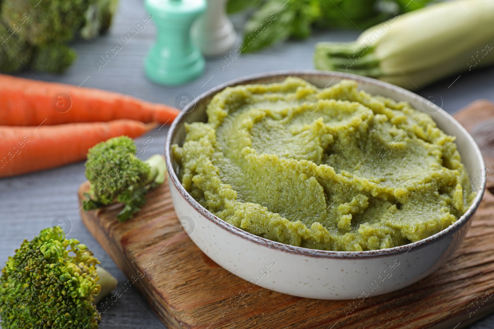 Photo of Bowl with tasty green puree and ingredients on light blue wooden table, closeup
