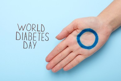 Woman showing palm with drawn blue circle near text World Diabetes Day on color background, top view