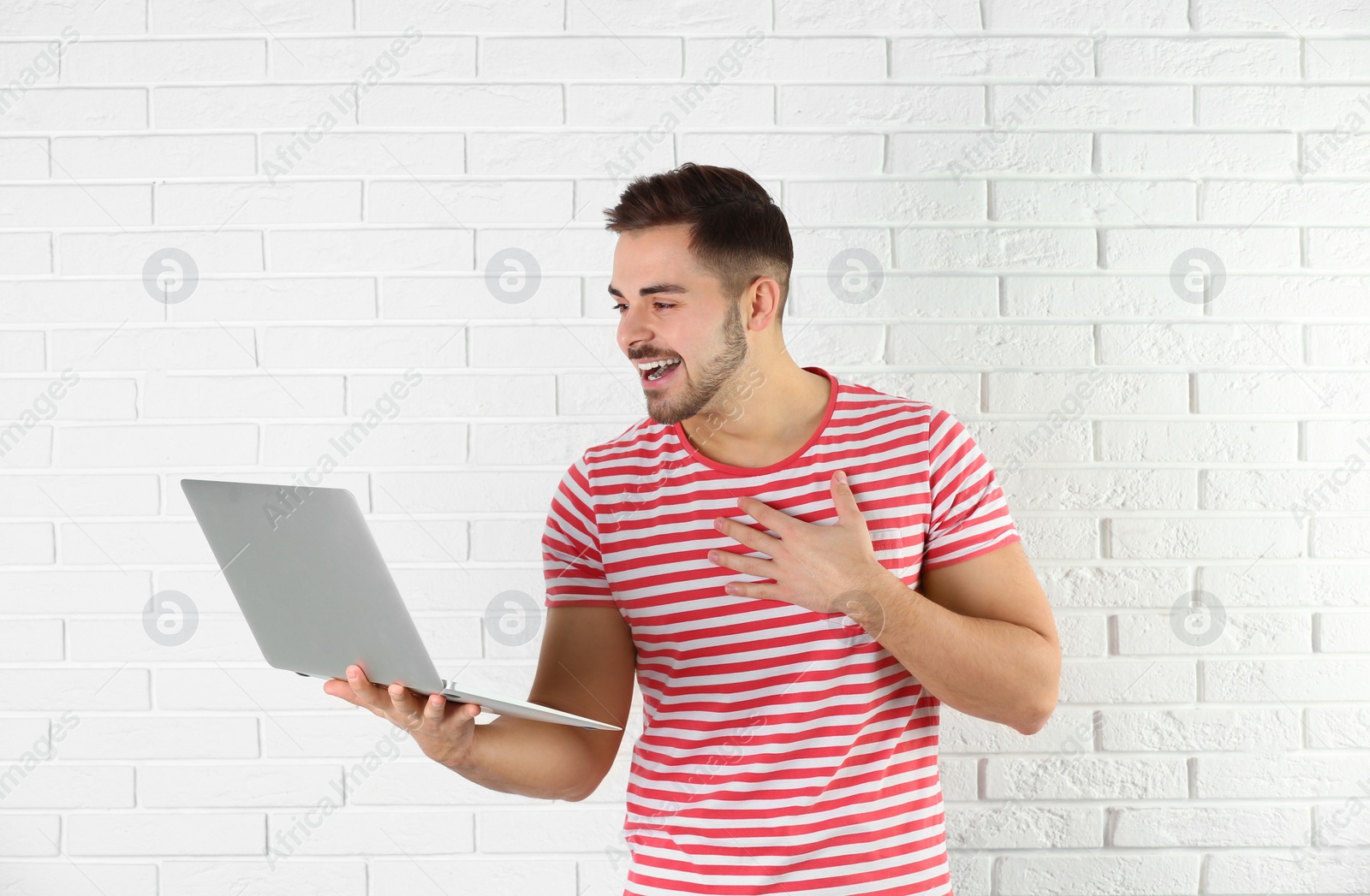 Photo of Man using laptop for video chat against brick wall