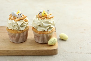 Tasty Easter cupcakes with vanilla cream and candies on gray table, space for text