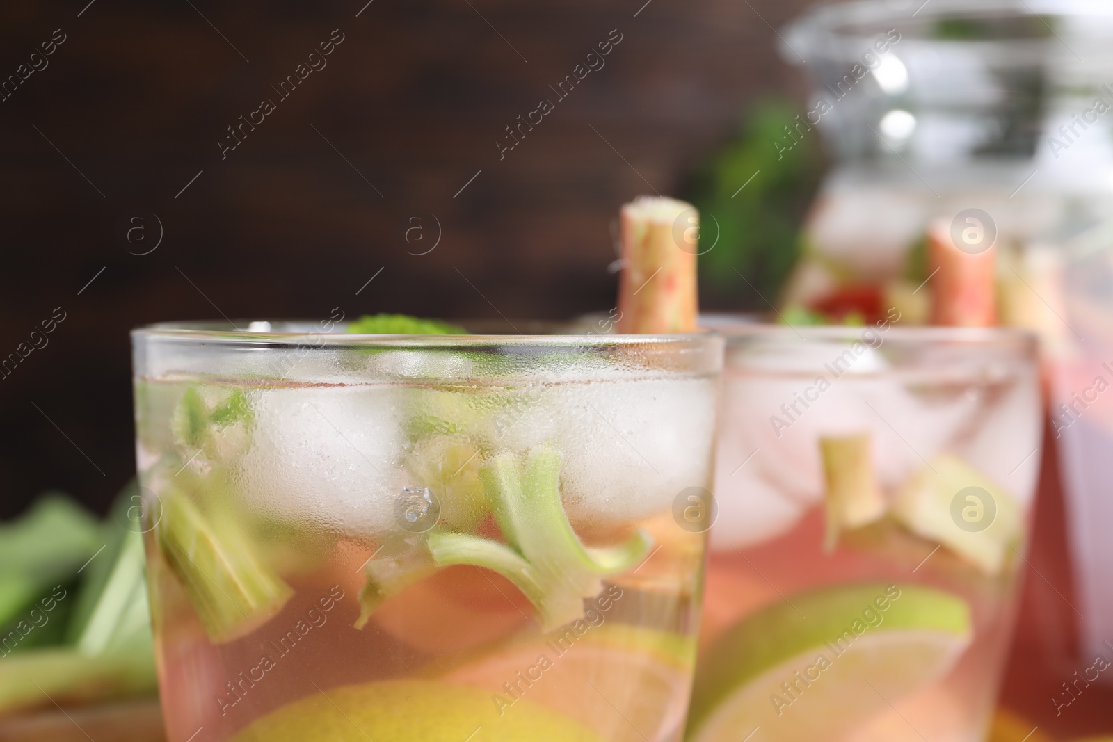 Photo of Glasses of tasty rhubarb cocktail with citrus fruits on blurred background, closeup