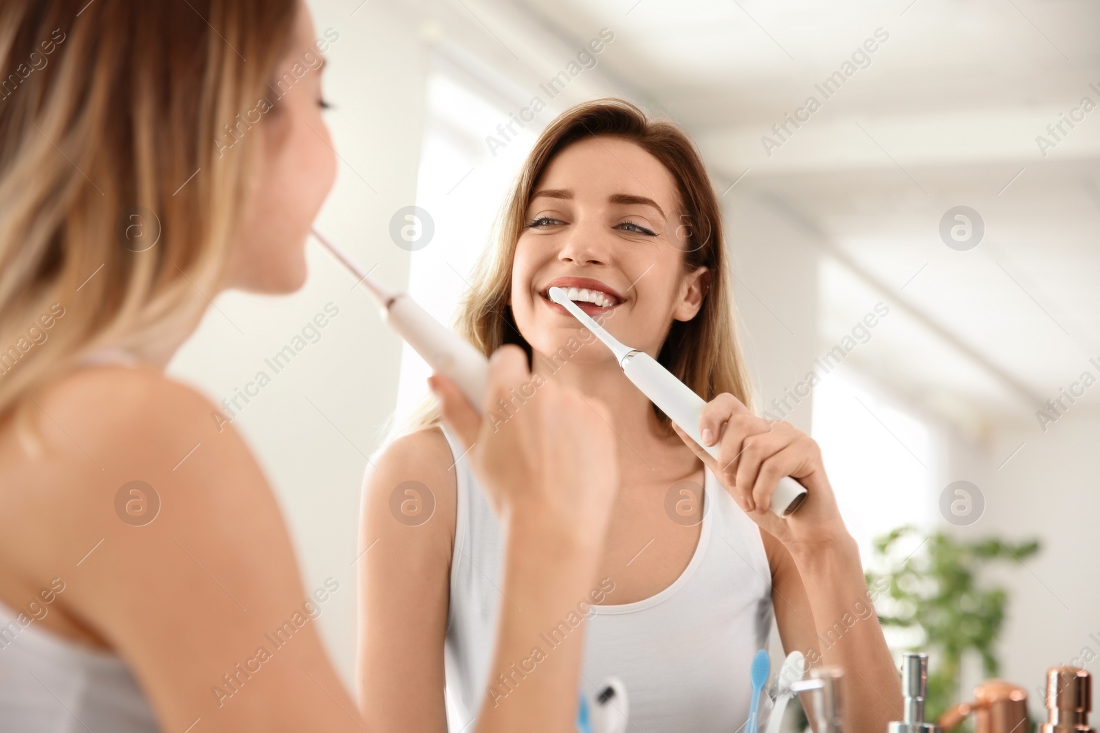 Photo of Young beautiful woman with toothbrush near mirror in bathroom. Personal hygiene