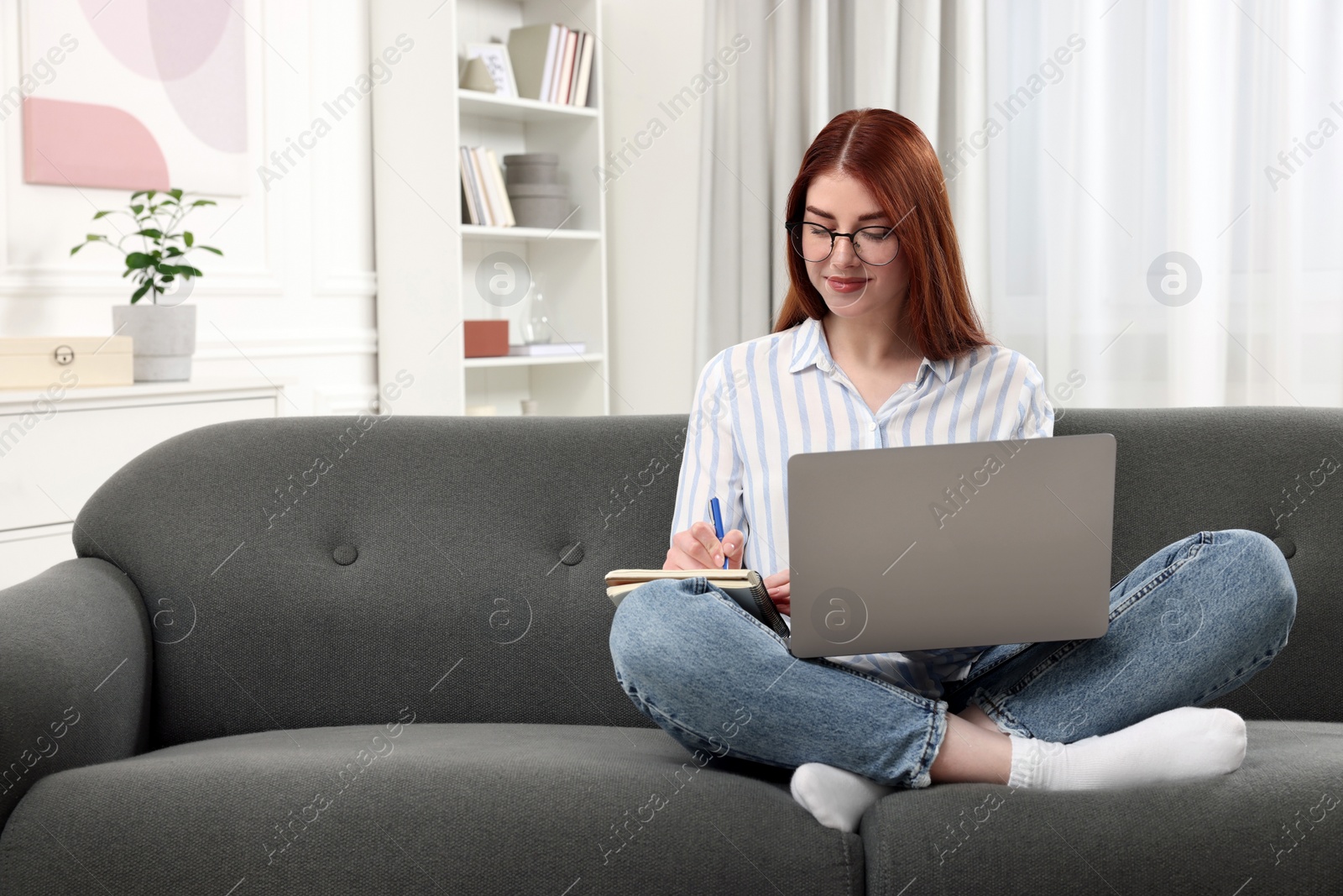 Photo of Beautiful woman with laptop writing notes on couch in room