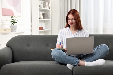 Photo of Beautiful woman with laptop writing notes on couch in room