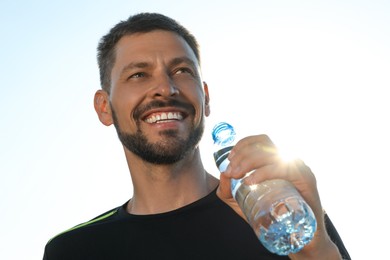Happy man with bottle of water outdoors on hot summer day. Refreshing drink