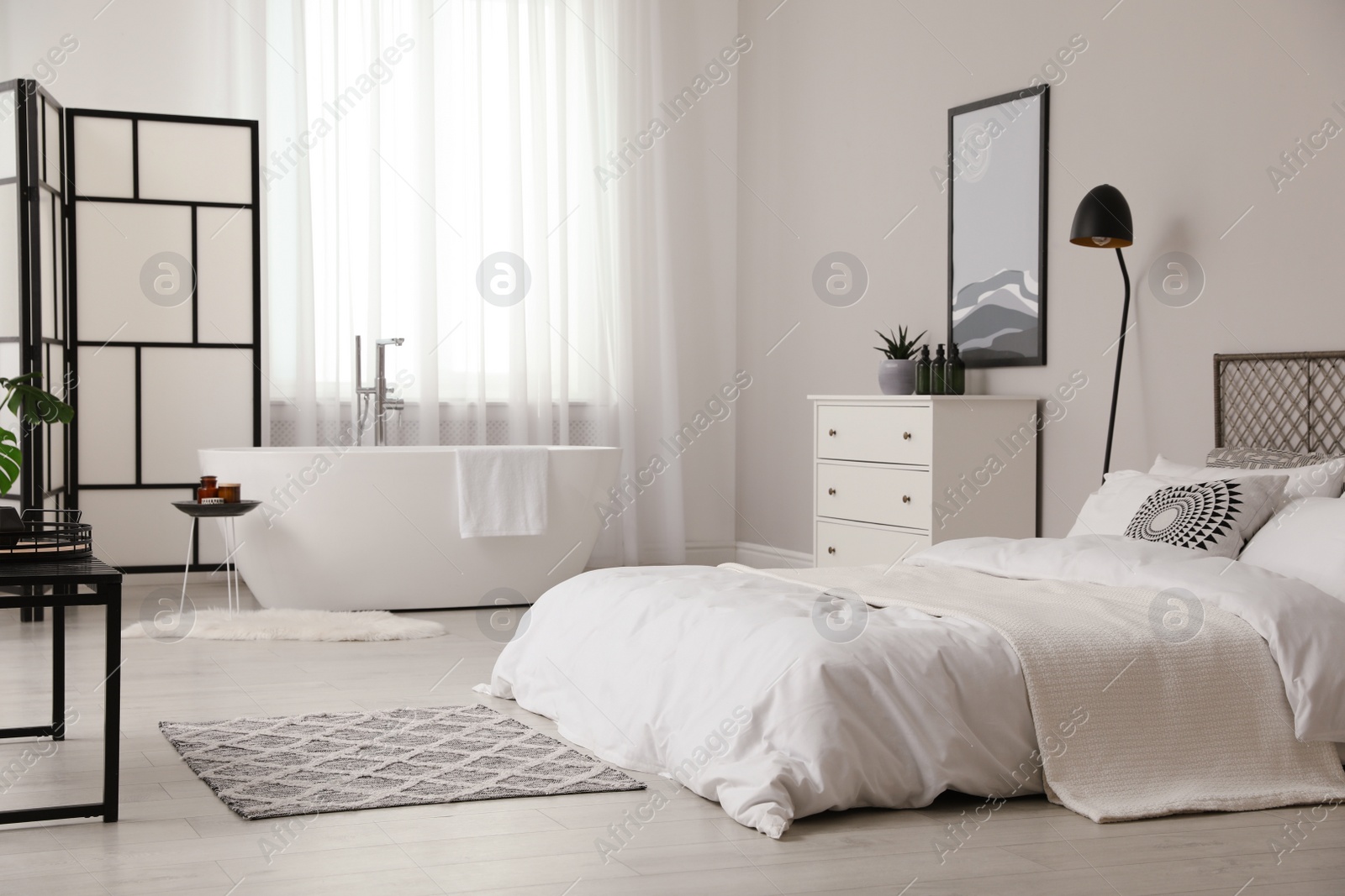 Photo of Stylish light apartment interior with white bathtub and bed