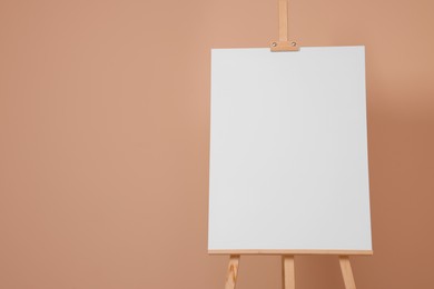 Photo of Wooden easel with blank canvas on beige background. Space for text