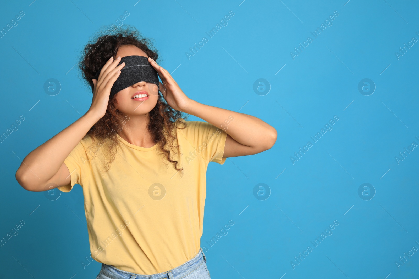 Photo of Young African-American woman with black blindfold on blue background