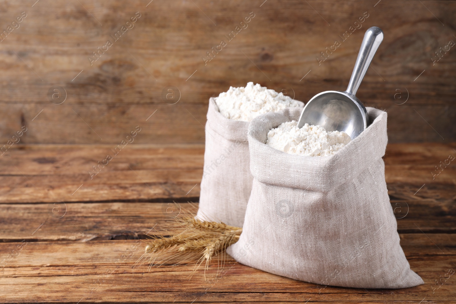 Photo of Sacks with flour and wheat spikes on wooden background. Space for text