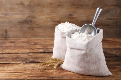 Photo of Sacks with flour and wheat spikes on wooden background. Space for text