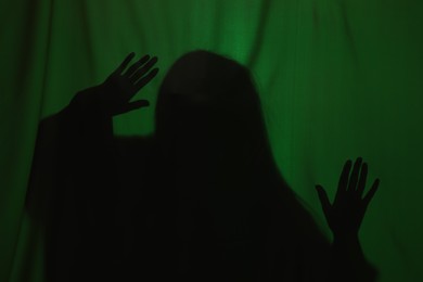 Photo of Silhouette of creepy ghost behind dark green cloth