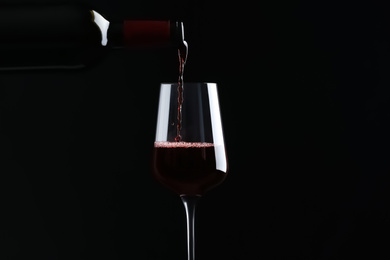 Photo of Pouring red wine from bottle into glass on black background