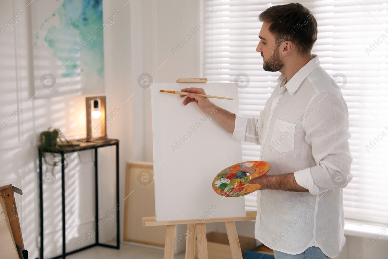 Photo of Young man painting on easel with brush in artist studio