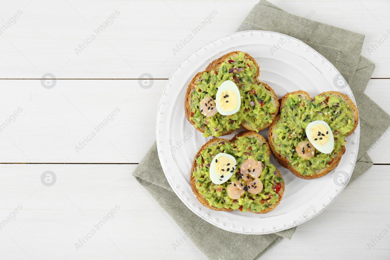 Photo of Slices of bread with tasty guacamole, eggs and shrimp on white wooden table, top view. Space for text