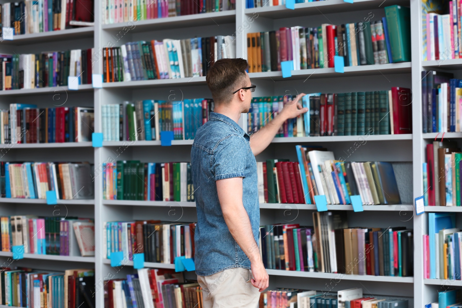 Photo of Young man taking book from shelving unit in library