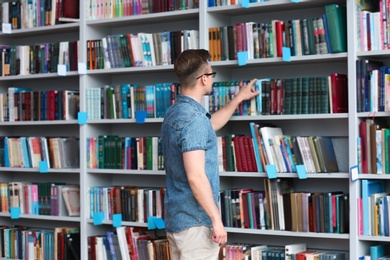 Photo of Young man taking book from shelving unit in library