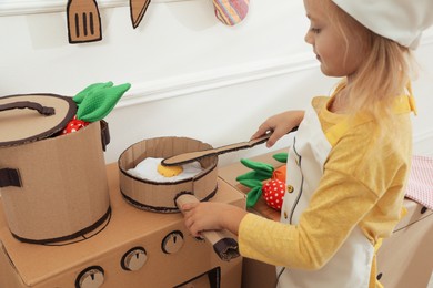 Photo of Little girl playing with toy cardboard kitchen indoors, closeup