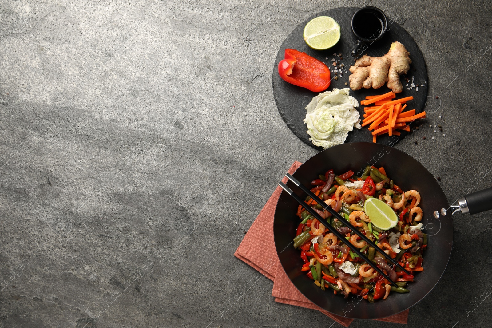 Photo of Shrimp stir fry with vegetables in wok and chopsticks on grey table, flat lay. Space for text