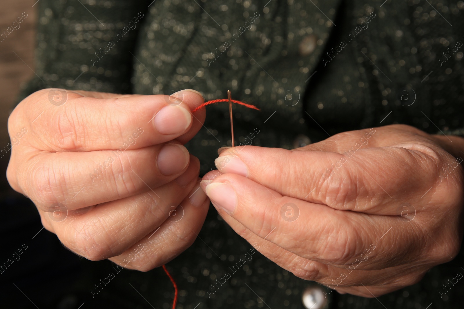 Photo of Closeup view of woman threading needle indoors. Sewing equipment