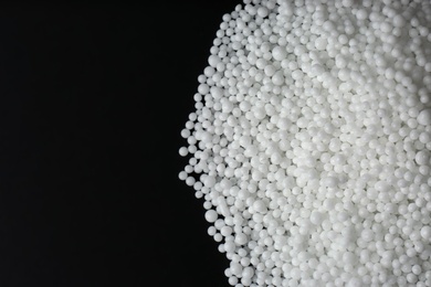 Photo of Pellets of ammonium nitrate on black background, flat lay with space for text. Mineral fertilizer