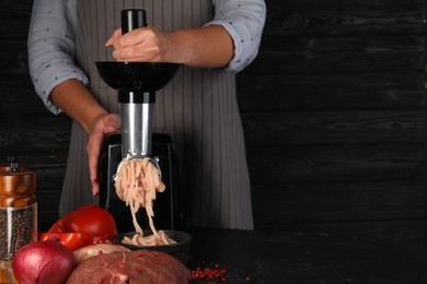 Woman making chicken mince with electric meat grinder at black table, closeup. Space for text