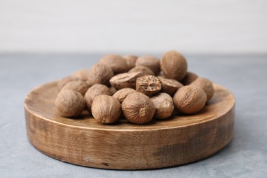 Photo of Wooden board with nutmegs on light grey table, closeup
