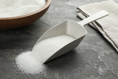 Granulated sugar in scoop on grey textured table, closeup