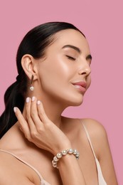 Photo of Young woman wearing elegant pearl jewelry on pink background