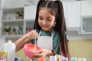 Photo of Cute little girl mixing ingredients with silicone spatula at table in kitchen. DIY slime toy