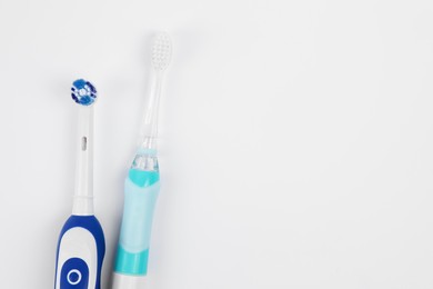 Electric toothbrushes on white background, flat lay. Space for text