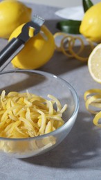 Bowl with peel pieces, fresh lemons and zester on grey table, closeup