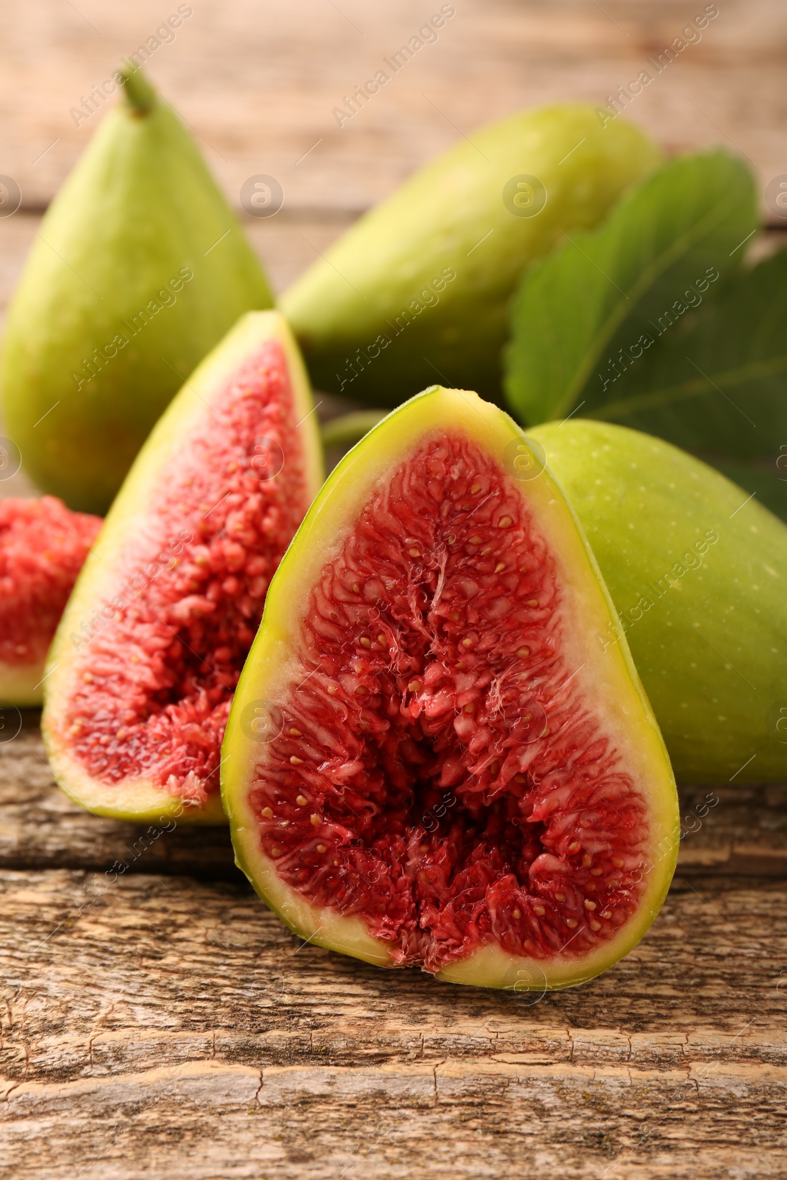 Photo of Cut and whole green figs on wooden table, closeup