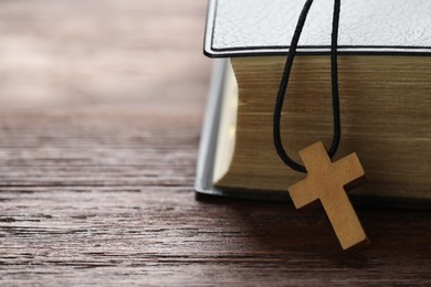 Photo of Wooden Christian cross and Bible on table, closeup. Space for text