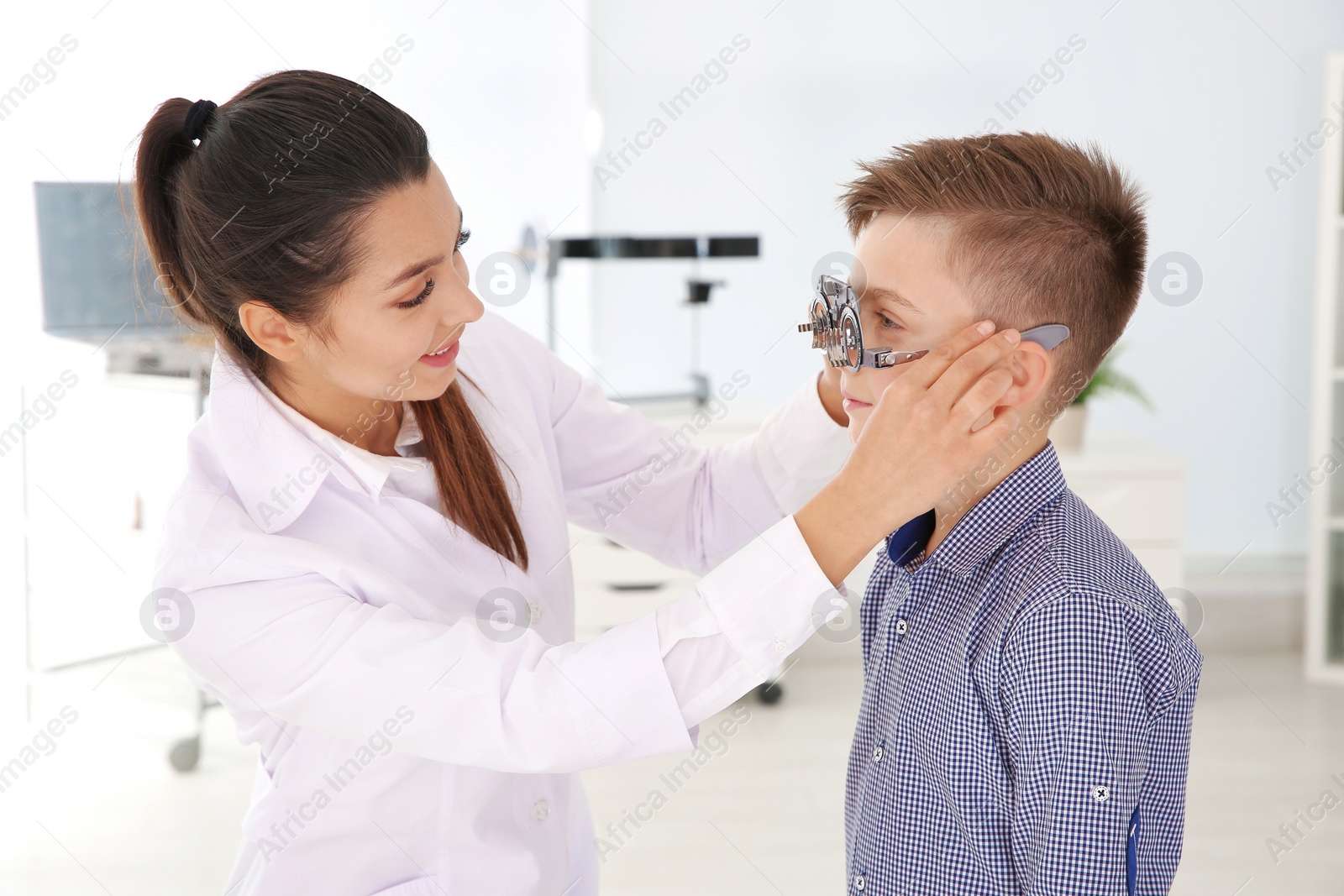 Photo of Children's doctor putting trial frame on little boy in clinic. Eye examination