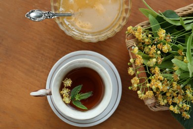 Cup of hot aromatic herbal tea, honey and linden blossoms on wooden table, flat lay