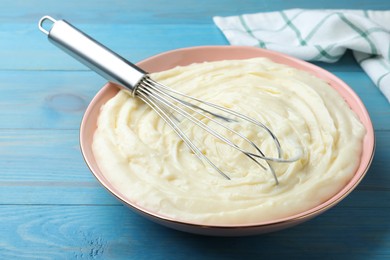 Photo of Pastry cream with balloon whisk on light blue wooden table, closeup