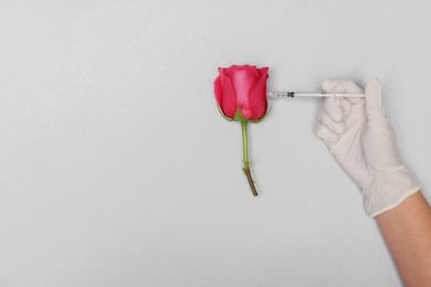 Doctor making injection to rose on light grey background, top view. Space for text