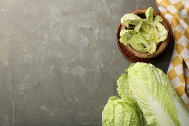 Photo of Fresh ripe Chinese cabbages and green leaves in bowl on gray textured table, flat lay. Space for text