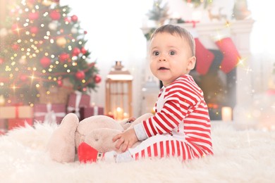 Image of Cute baby playing with toy on floor in room decorated for Christmas. Magical festive atmosphere