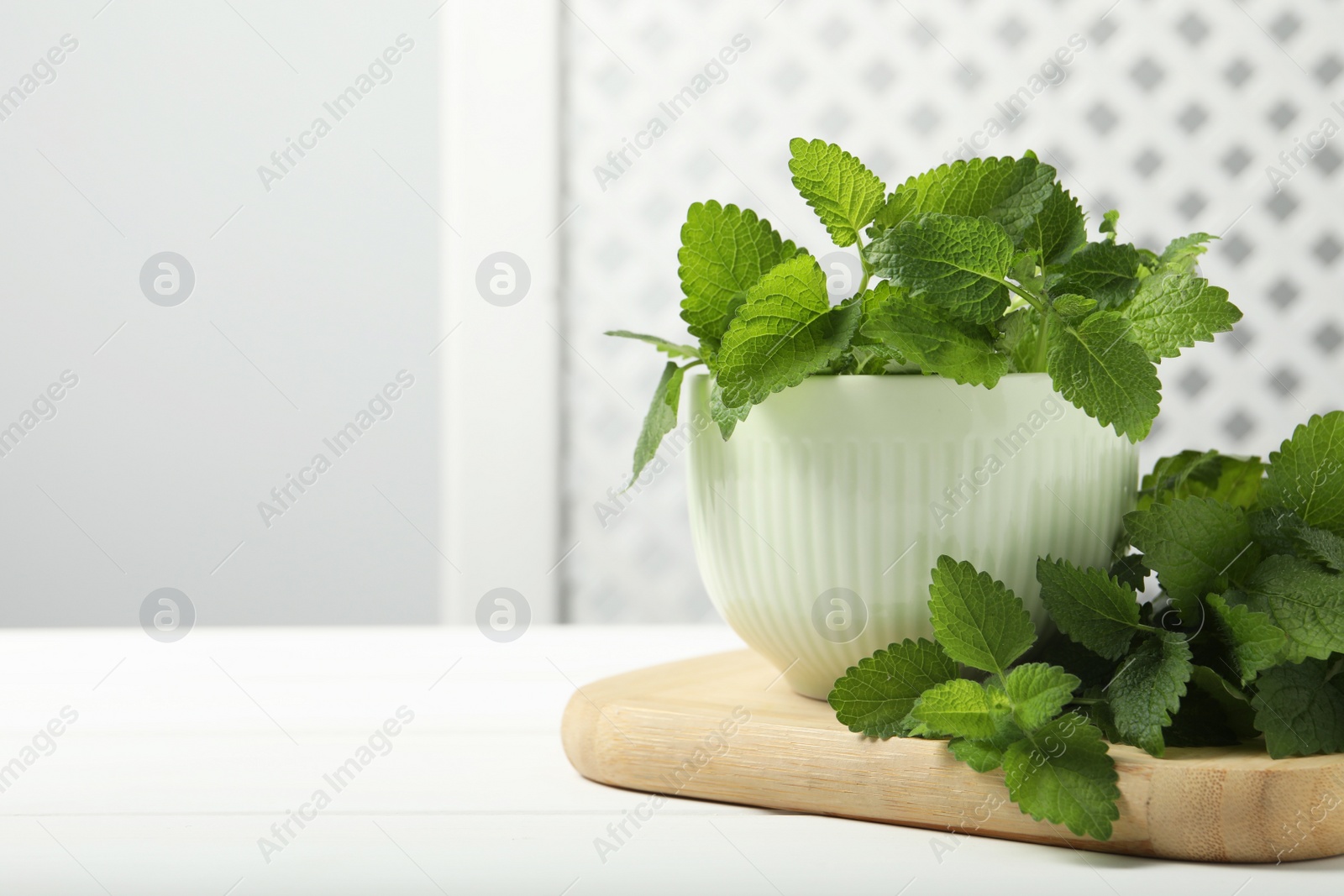 Photo of Fresh lemon balm in bowl on white wooden table, space for text