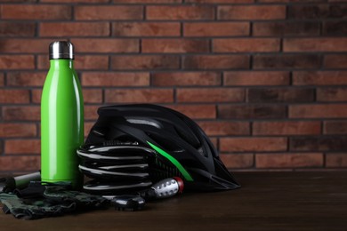 Photo of Different cycling accessories on wooden table against brick wall, space for text