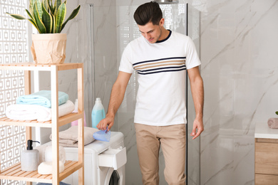 Photo of Man pouring laundry detergent into washing machine drawer in bathroom