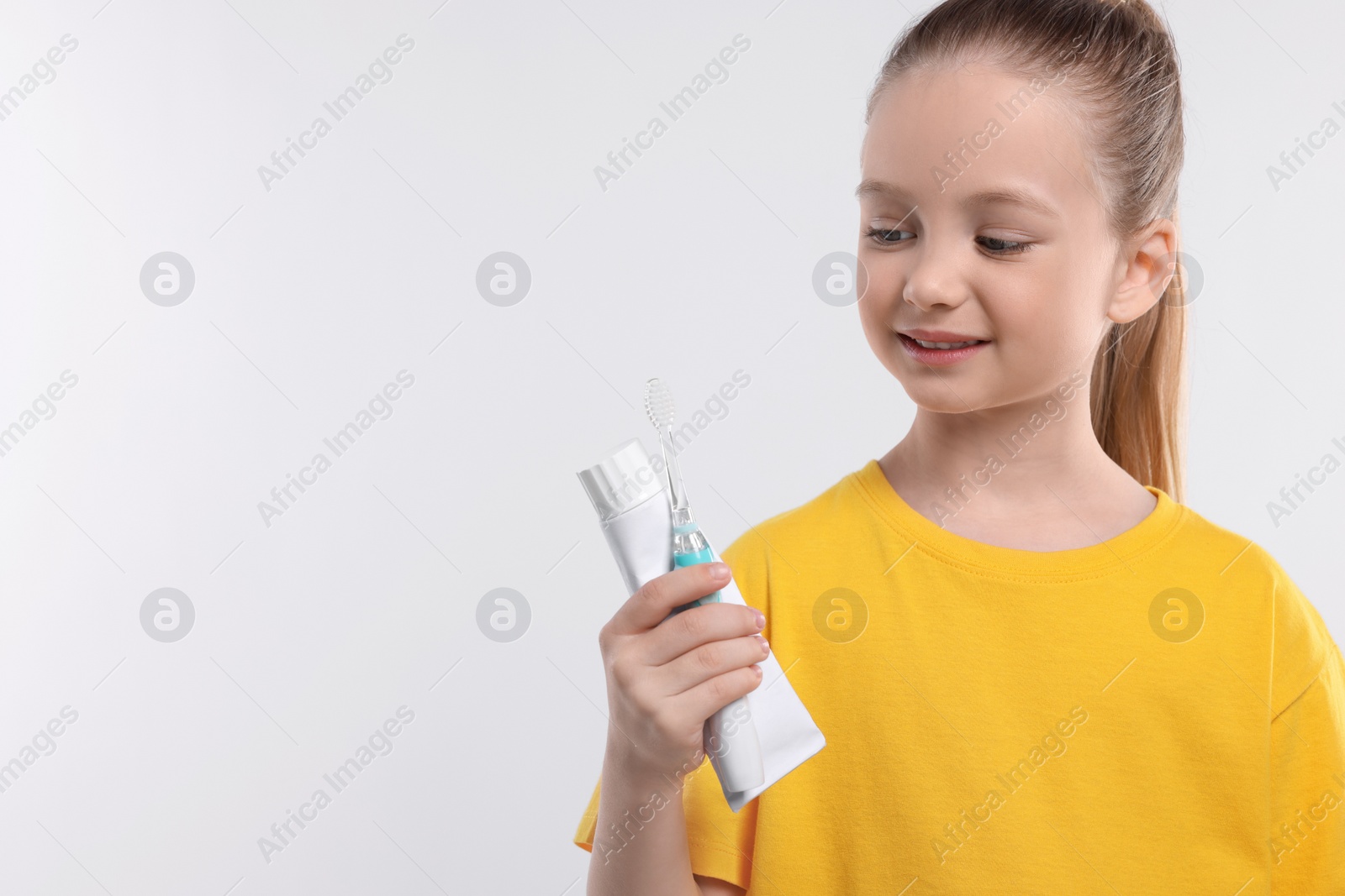 Photo of Happy girl holding electric toothbrush and tube of toothpaste on white background. Space for text