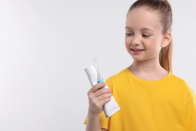 Happy girl holding electric toothbrush and tube of toothpaste on white background. Space for text