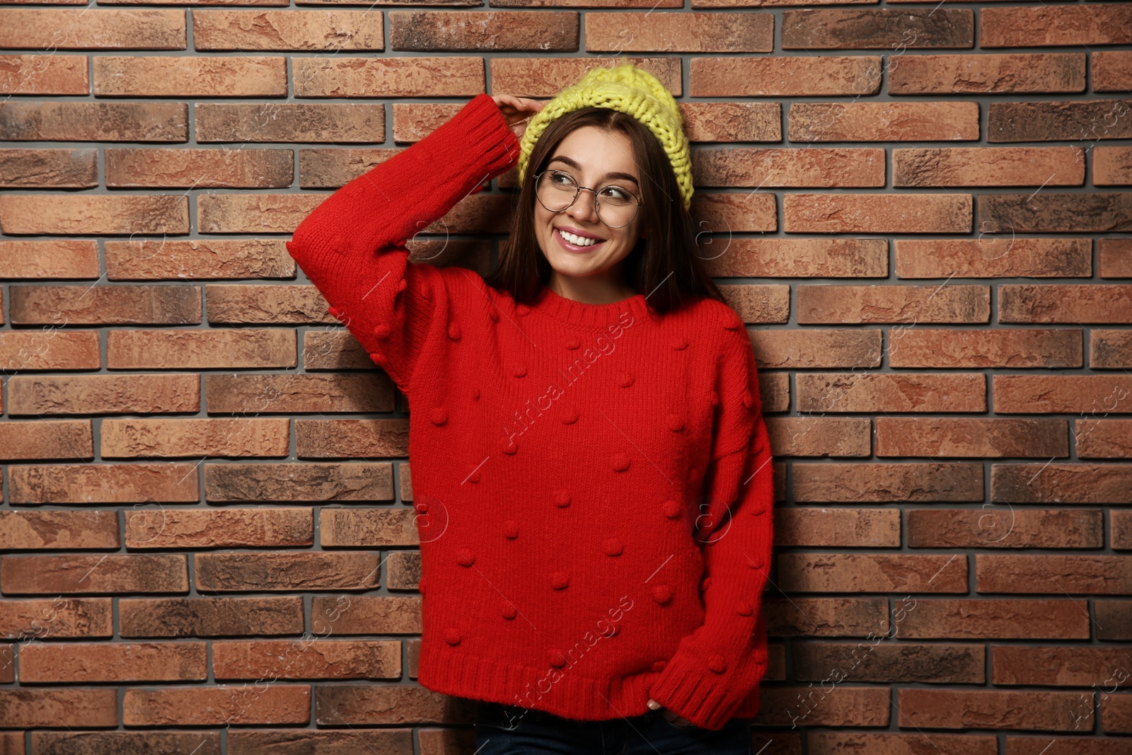 Photo of Beautiful young woman in warm sweater with hat near brick wall