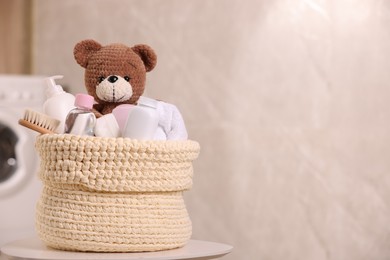Knitted basket with baby cosmetic products, bath accessories and toy bear on white table indoors. Space for text