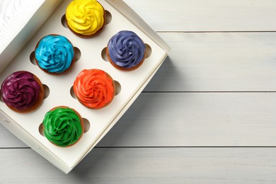 Box with different cupcakes on white wooden table, top view. Space for text