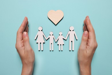 Photo of Woman protecting figures of family and heart on light blue background, top view. Insurance concept