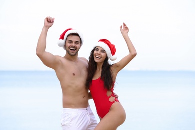 Happy young couple with Santa hats together on beach